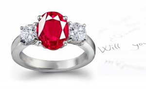 Three Stone Ruby Engagement Ring: Platinum ruby diamond ring set with center oval ruby and side diamond rounds.
